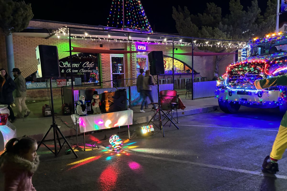People gathered outside a downtown cafe as lit vehicles pass